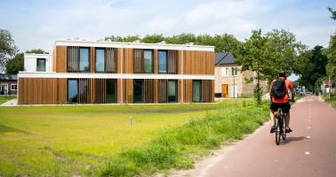 Een fietser passeert een houten wooncomplex met daarachter stenen woningen