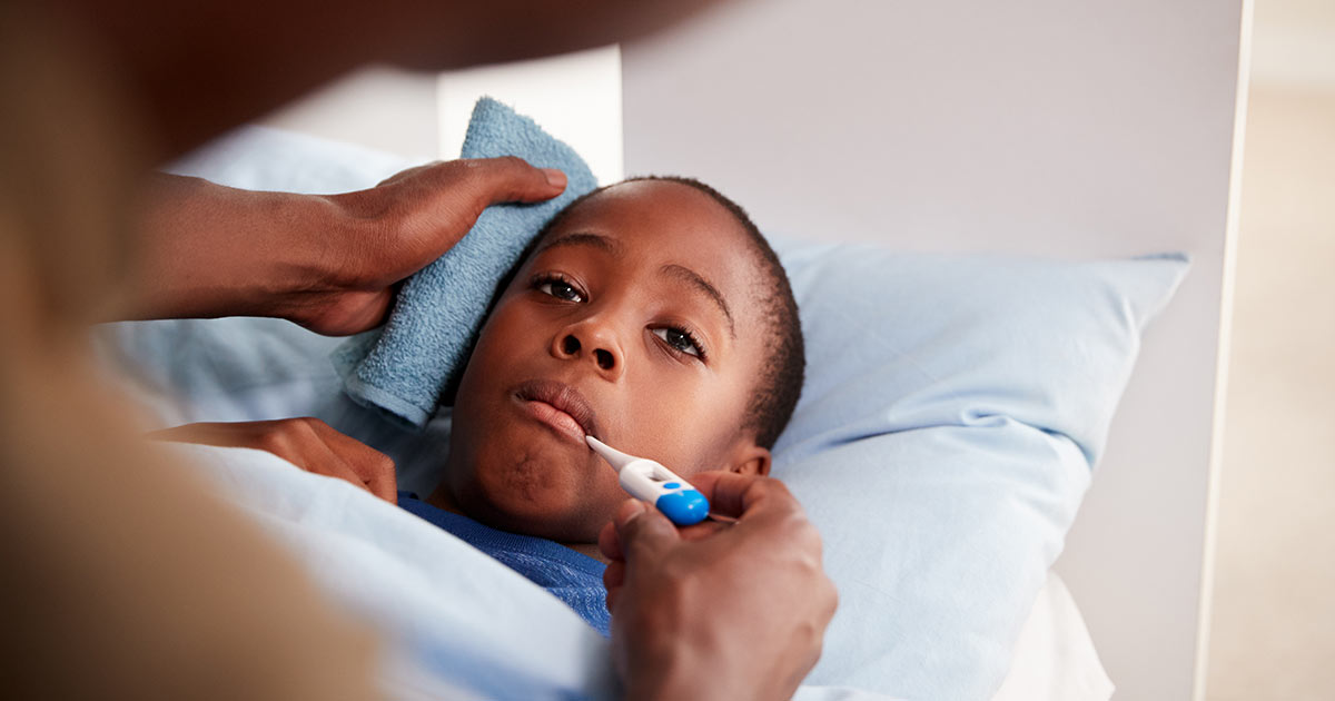 A child lying in bed, being checked for fever with a thermometer.