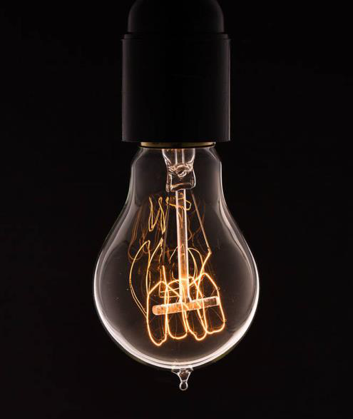 An incandescent light bulb filament glowing brightly inside a glass bulb