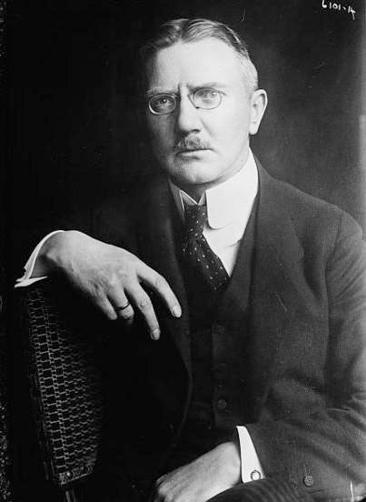 A black and white portrait of a man with glasses, wearing a suit and tie.