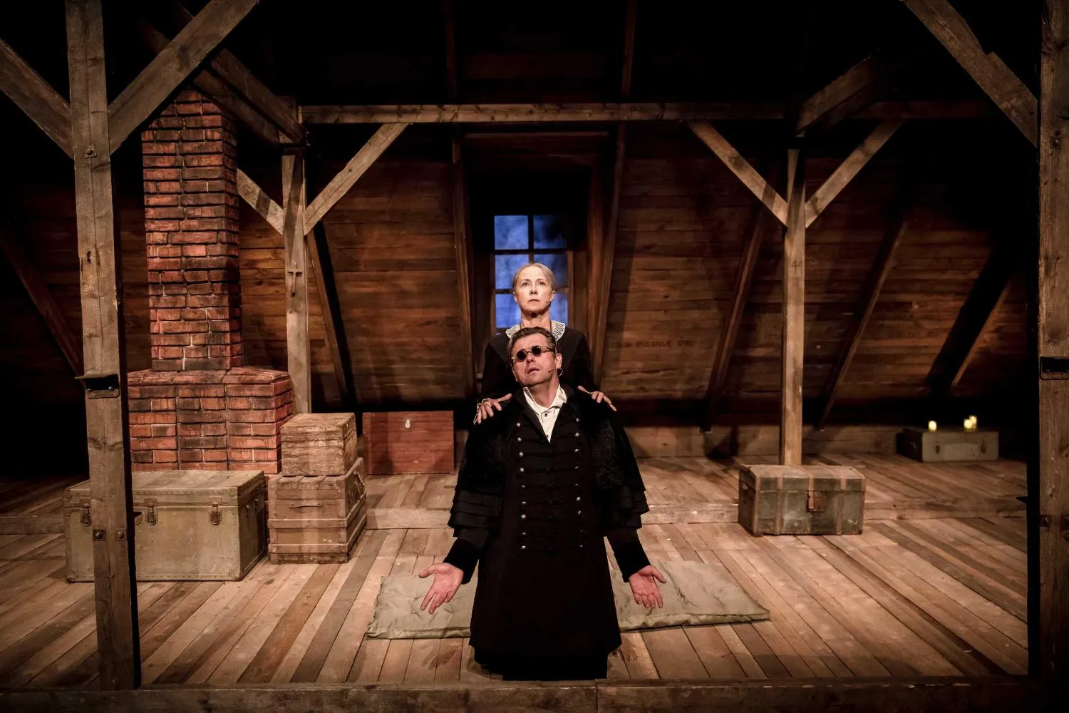 Towiański (Maciej Konopiński) klęczy na środku sceny z rozłożonymi dłońmi. Żona (Joanna Kreft-Baka) stoi za nim i kładzie ręce na jego ramionach. W tle stoją skrzynie.