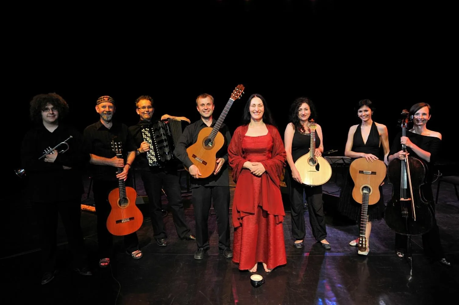 Marzena Nieczuja Urbańska z zespołem muzyków w rzędzie. Od lewej: flecista, gitarzysta, akordeonista, gitarzysta, Marzena Nieczuja Urbańska, kitarzystka, gitarzystka i skrzypaczka. Patrzą na wprost i uśmiechają się.
