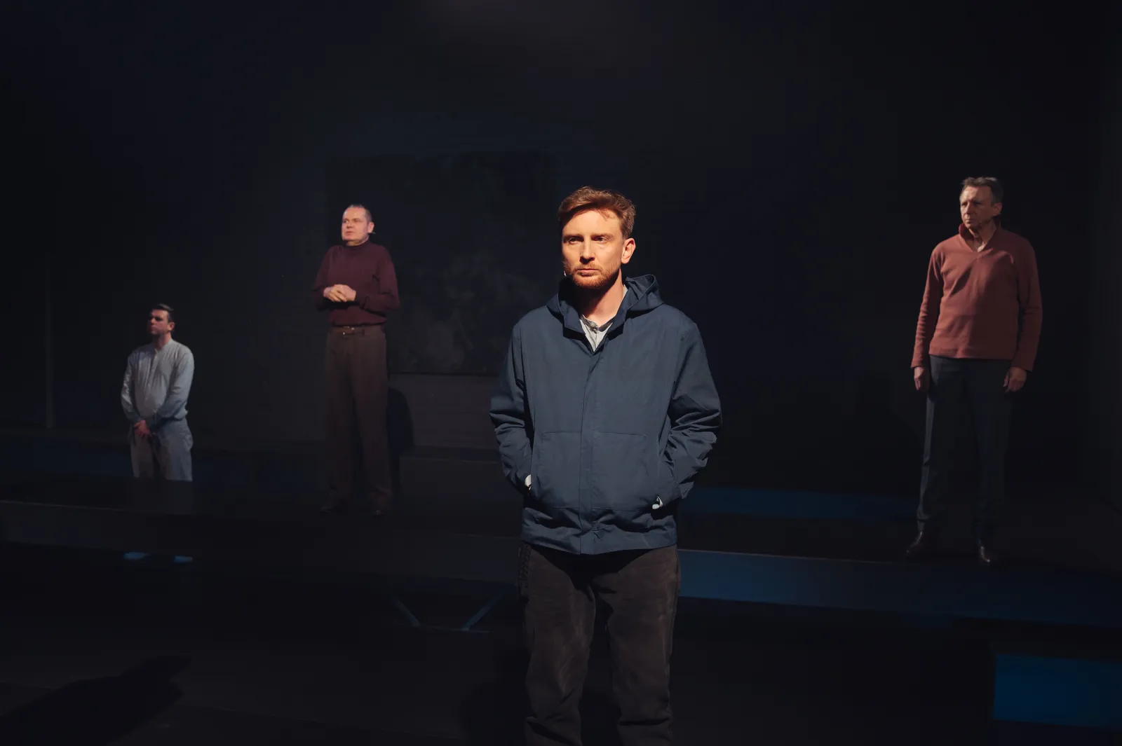 Czterech mężczyzn wyłania się z mroku. Z przodu Piotr Biedroń z rękami w kieszeniach granatowej bluzy. W tle Cezary Rybiński, Jarosław Tyrański ze splecionymi na piersi dłońmi i Maciej Konopiński ze splecionymi w dole dłońmi.