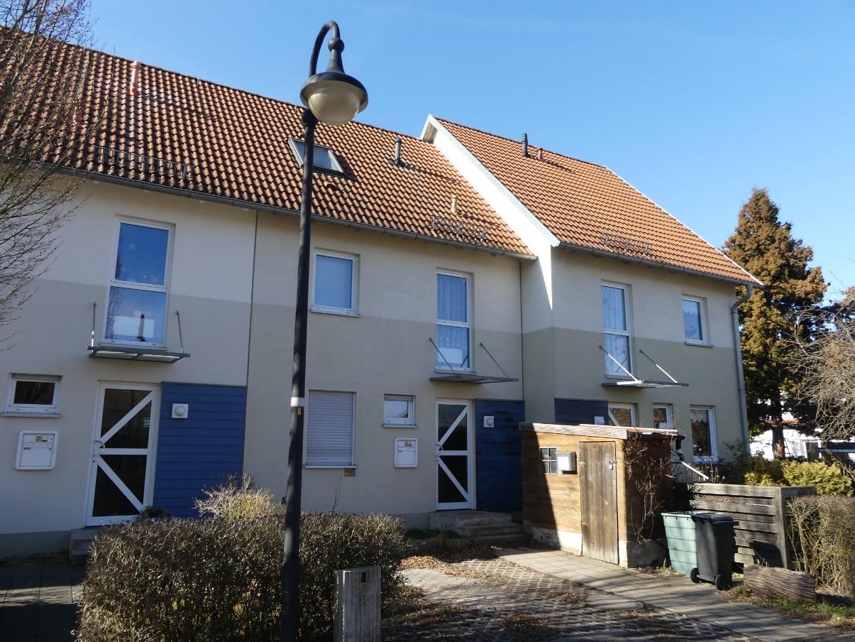 Zweistöckiges Reihenmittelhaus mit Satteldach, hellen Fassaden und blauen Türen, vorne mit Straßenlaterne und gepflastertem Weg