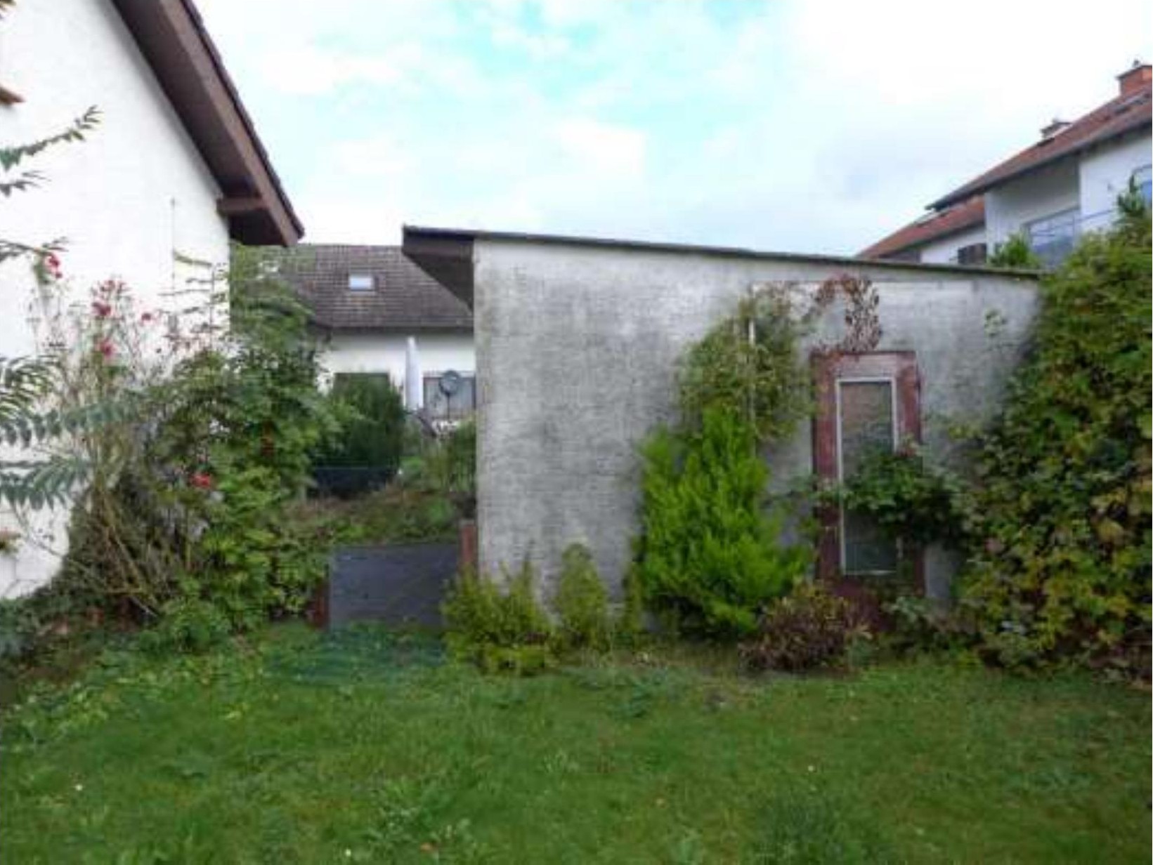 Gartenbereich mit Gras, Sträuchern und einer Betonwand, Teil eines Zweifamilienhauses in Bad Nauheim