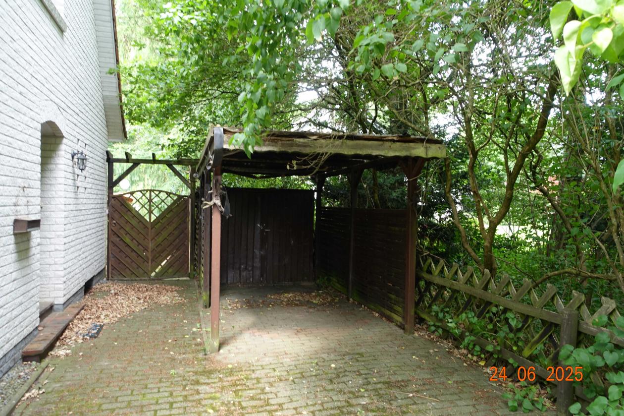 Gartenbereich mit Pergola, Holztor und Bepflanzung neben einem weißen Backsteinhaus