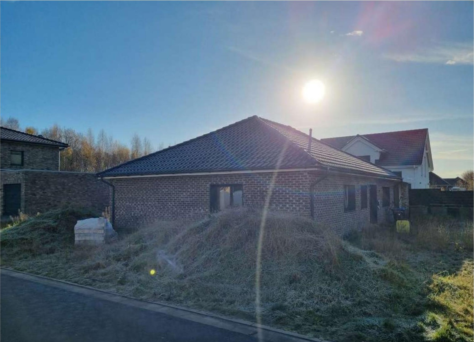 Einfamilienhaus aus Ziegelsteinen mit Satteldach, Seitenansicht mit frostbedecktem Garten und angrenzenden Gebäuden im Hintergrund
