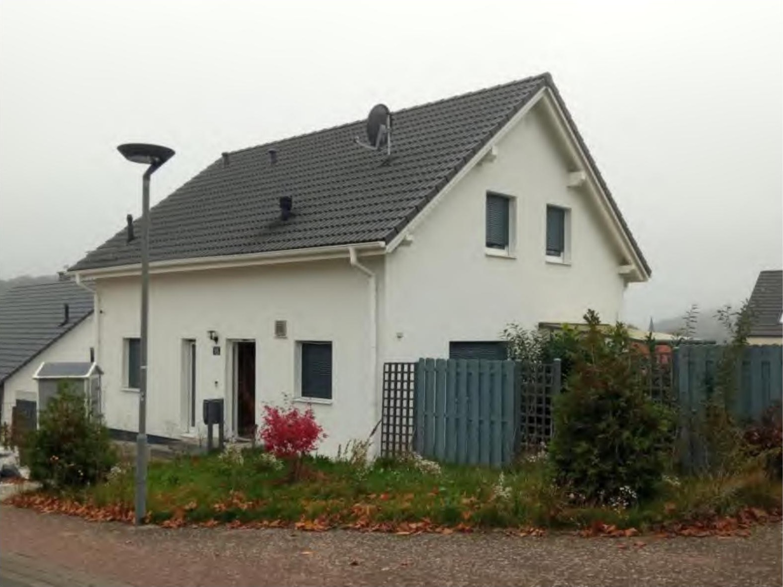 Einfamilienhaus in Schotten, Zum Eisenacker 15, mit weißer Fassade, grauem Dach und Vorgarten mit Büschen und Laub