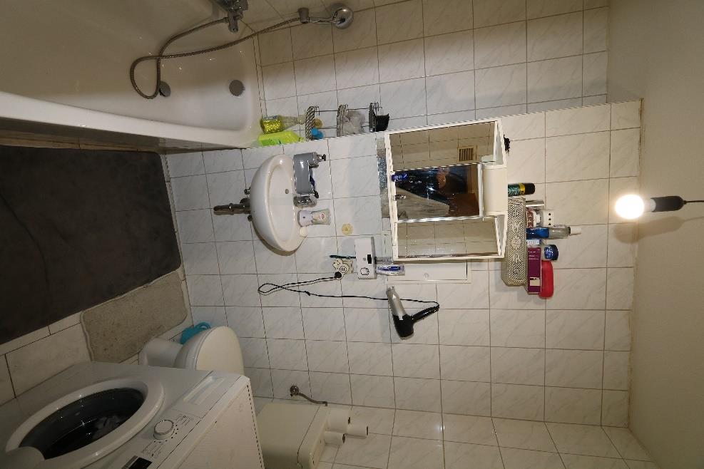 Badezimmer mit weiß gefliesten Wänden, Waschbecken, Spiegelschrank, Dusche, Toilette und Waschmaschine. Aufbewahrungselemente und Haushaltsgegenstände sind sichtbar