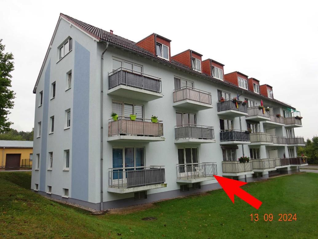 Seitenansicht eines mehrstöckigen Wohngebäudes mit Balkonen, Fenstern und Dachgauben auf einem Grünstreifen