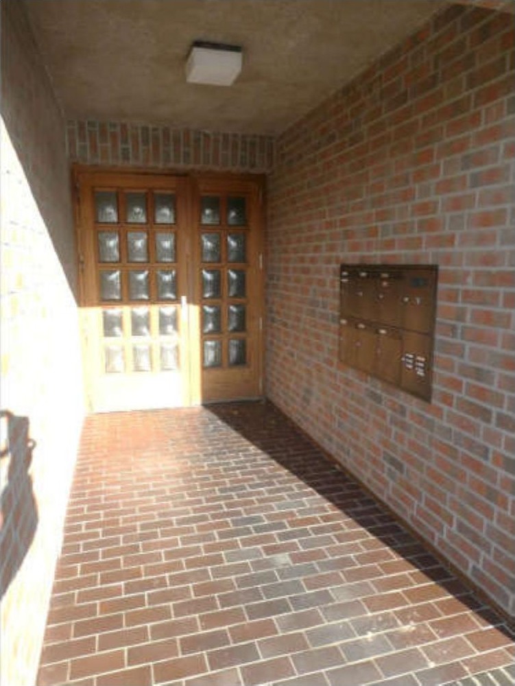 Eingangsbereich mit Holztür, Glasfeldern, Backsteinwänden und -boden sowie Briefkastenanlage an der Wand