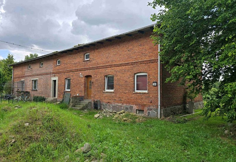 Einfamilienhaus aus rotem Backstein, Hermannshöhe 29, Gültz, 17089. Frontansicht mit Holztür, mehreren Fenstern, steinernem Sockel und Grünfläche im Vordergrund