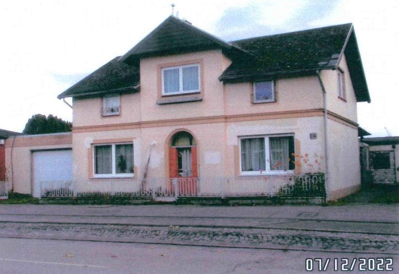 Zweistöckiges Mehrfamilienhaus in Lübeck, Schwartauer Allee 136, mit dunklem Satteldach, cremefarbener Fassade, Eingang mit roter Tür und Garagenanbau links