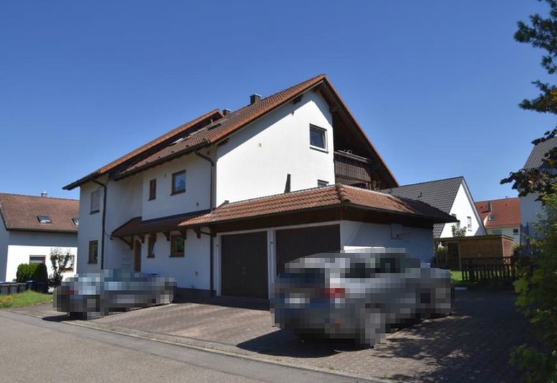 Vorderansicht eines Mehrfamilienhauses in Bondorf, Wengertsteig 6, mit weißer Fassade, braunem Satteldach und integriertem Carport. Zwei geparkte Fahrzeuge vor dem Haus