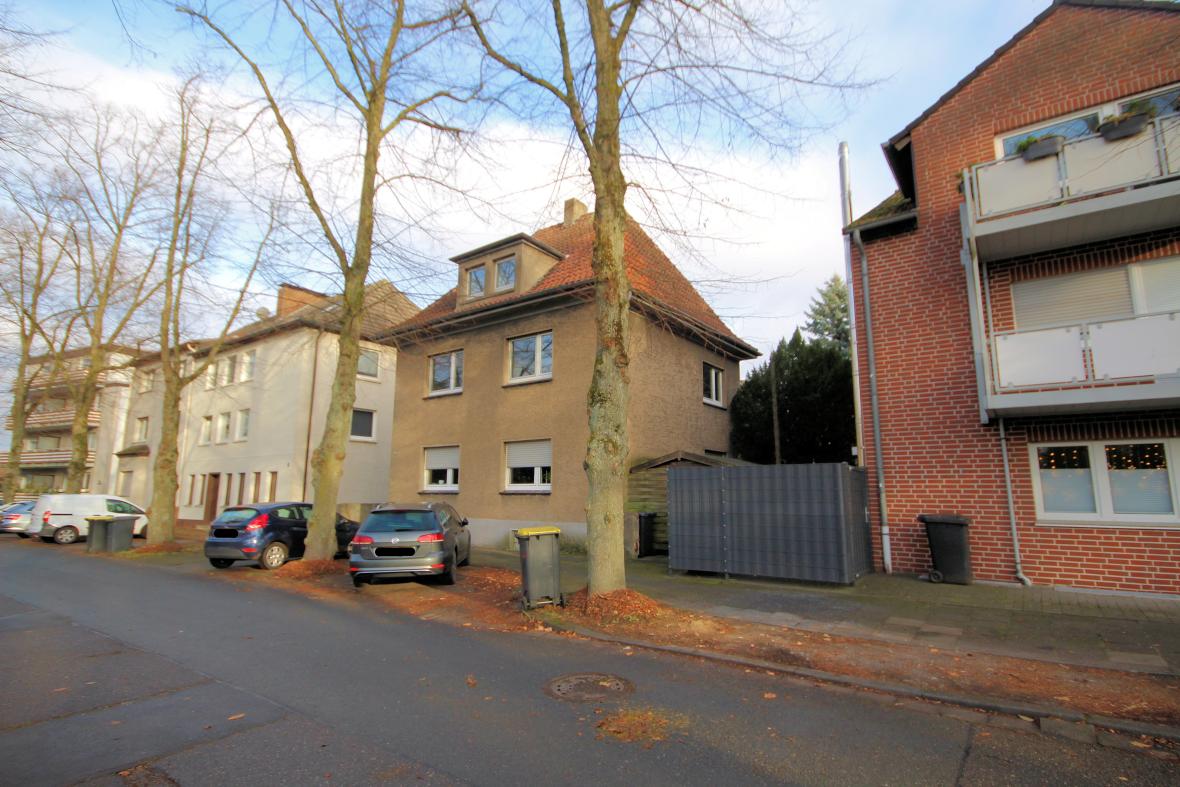 Seitenansicht eines Mehrfamilienhauses in Marl mit angrenzenden Gebäuden, Bäumen und geparkten Fahrzeugen an einer Straße