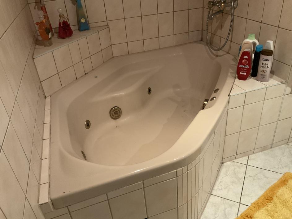 Badezimmer mit Eckbadewanne, Fliesenverkleidung und Pflegeprodukten auf der Ablage
