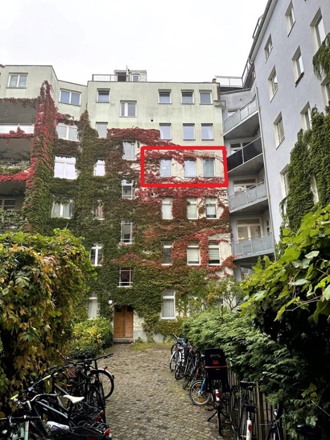 Rückansicht eines Mehrfamilienhauses mit Efeubewuchs, Innenhof mit Fahrrädern, Wohnung im roten Kasten hervorgehoben