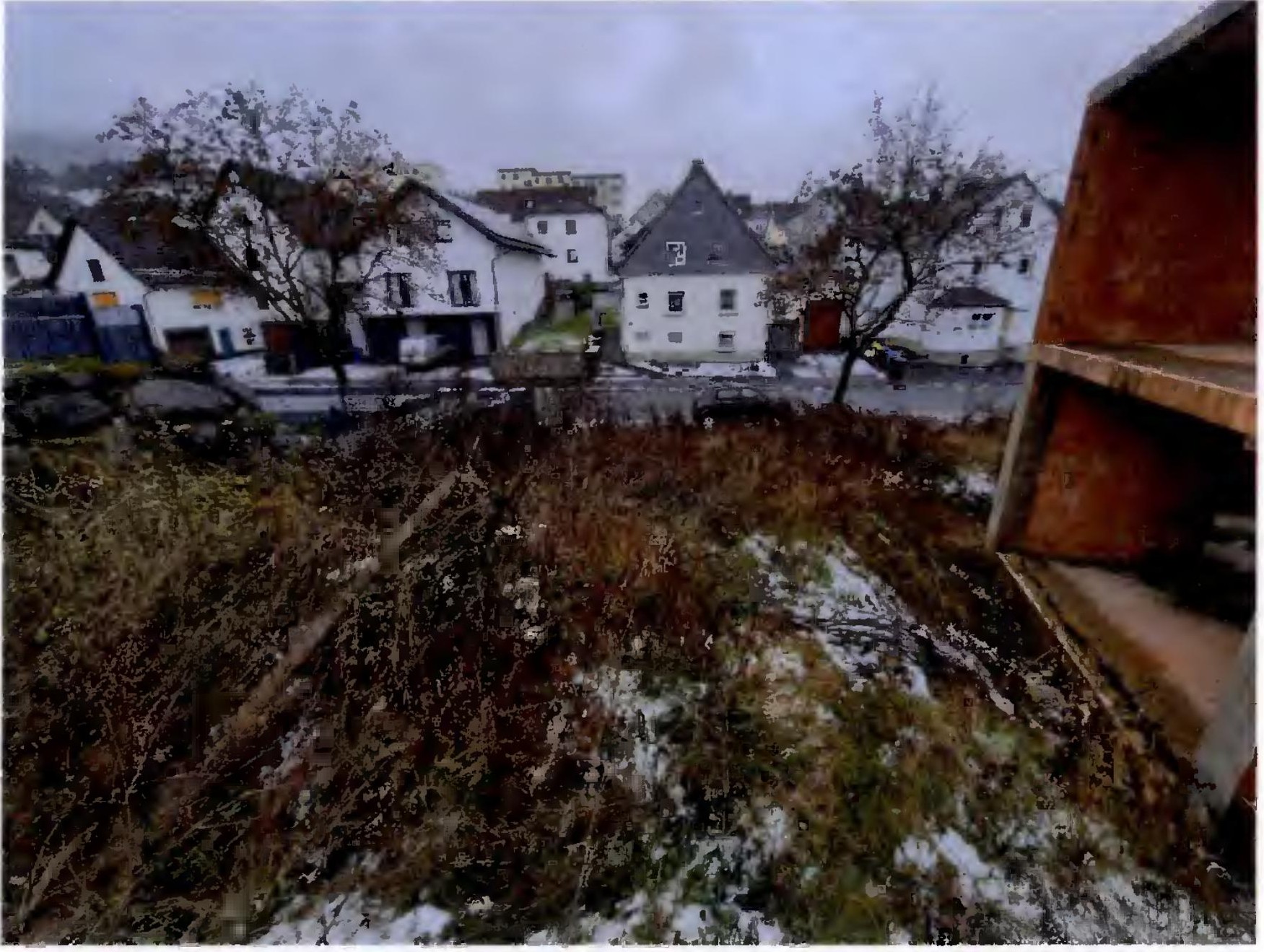 Überwuchertes Grundstück mit Schneeresten und Blick auf umliegende Gebäude in Breidenbach, Bachstraße 19
