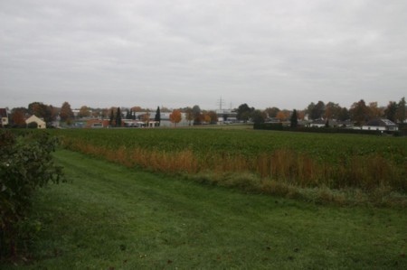 Unbebautes Grundstück in Ichenhausen, Nähe St.-Willibald-Weg, mit Grünfläche und Feldern, im Hintergrund Bäume und Gebäude unter bewölktem Himmel