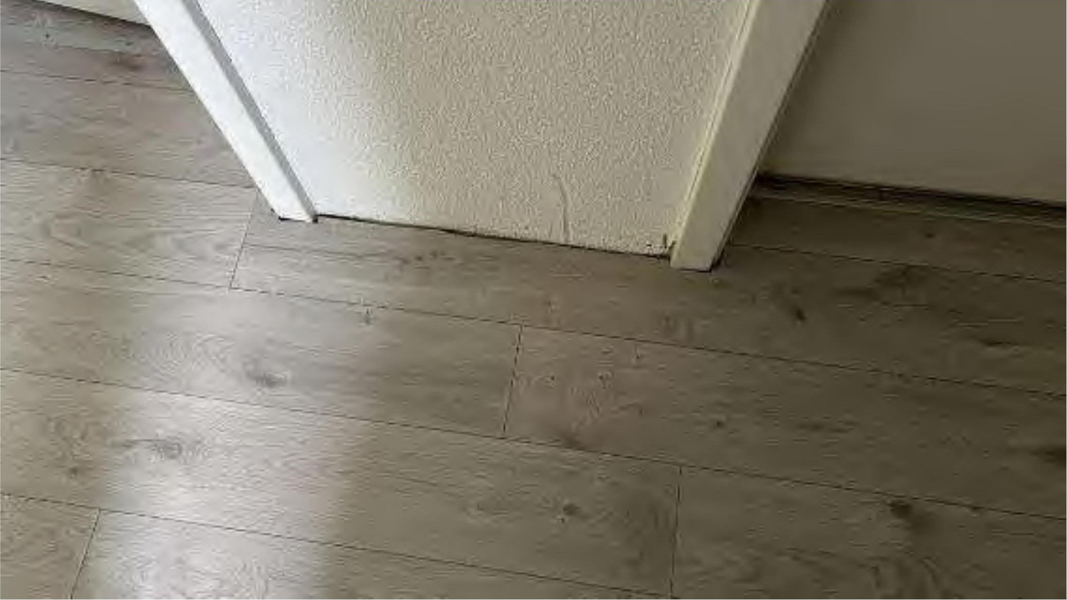 Blick auf einen hellgrauen Holzoptikboden neben einer weißen Wand mit Putzstruktur im Innenraum eines Einfamilienhauses