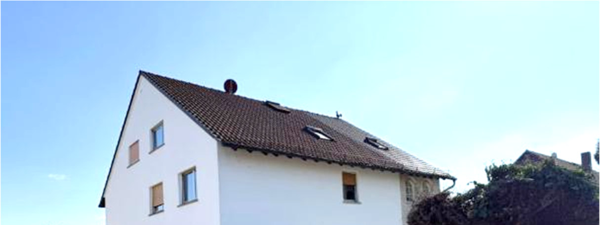 Seitenansicht eines weißen Gebäudes mit braunem Ziegeldach, mehreren Fenstern und Dachfenstern unter klarem Himmel