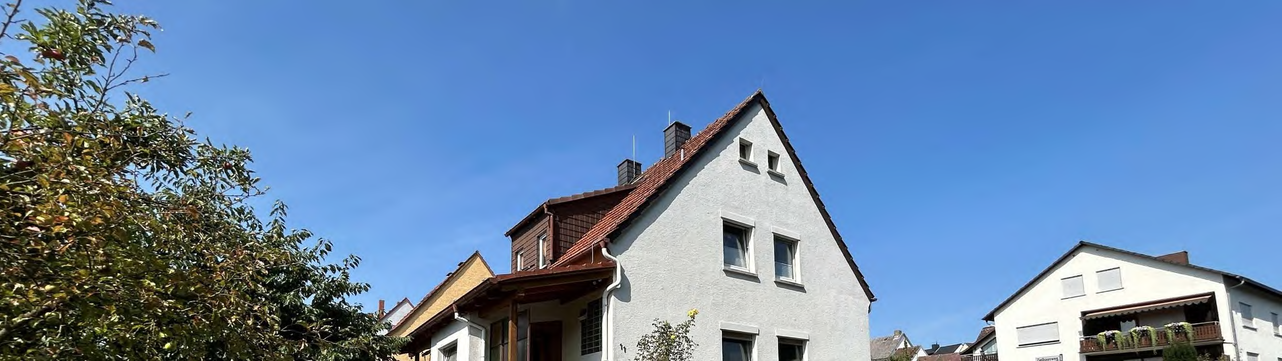Außenansicht eines Gebäudes an der Zielhausweg 11 in Wetzlar, 35582, mit grauer Fassade, rotem Dach und angrenzenden Häusern unter klarem Himmel