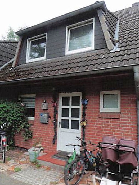 Reihenhaus in Halstenbek, Weidenstraße 13a, mit rotem Backsteinfassade, weißer Tür, Dachgauben und Ziegeldach. Fahrrad und Gartenmöbel vor dem Eingang