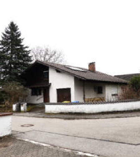 Einfamilienhaus in Markt Wald, Fuggerstr. 15, mit weißer Fassade, dunklem Satteldach und angrenzendem Hofbereich. Im Hintergrund Nadelbaum und kahle Bäume