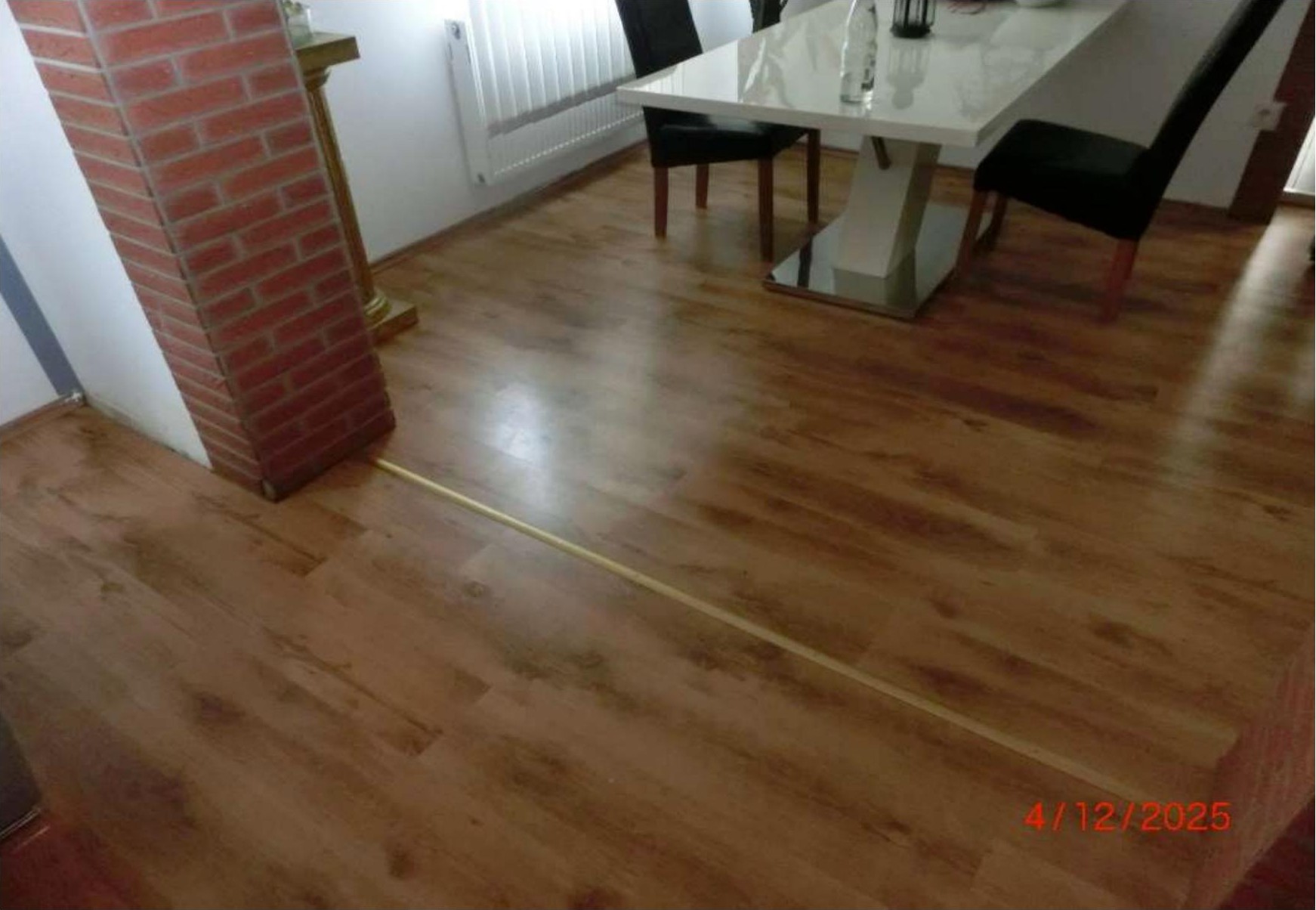 Innenraum mit Holzboden, weißer Esstisch, schwarzen Stühlen und Backsteinpfeiler im Wohnbereich eines Einfamilienhauses