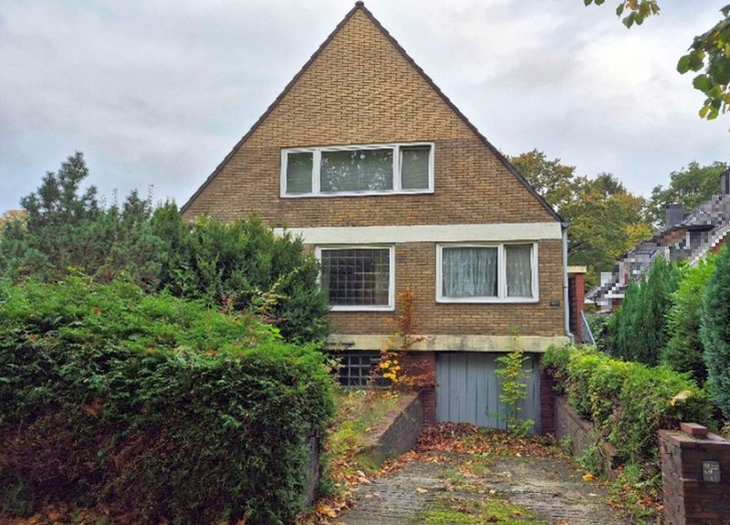 Einfamilienhaus in Hamburg, Pillauer Straße 103, 22047, mit braunem Ziegeldach, Fenstern im Obergeschoss und Einfahrt mit Garagentür, umgeben von Hecken und Laub