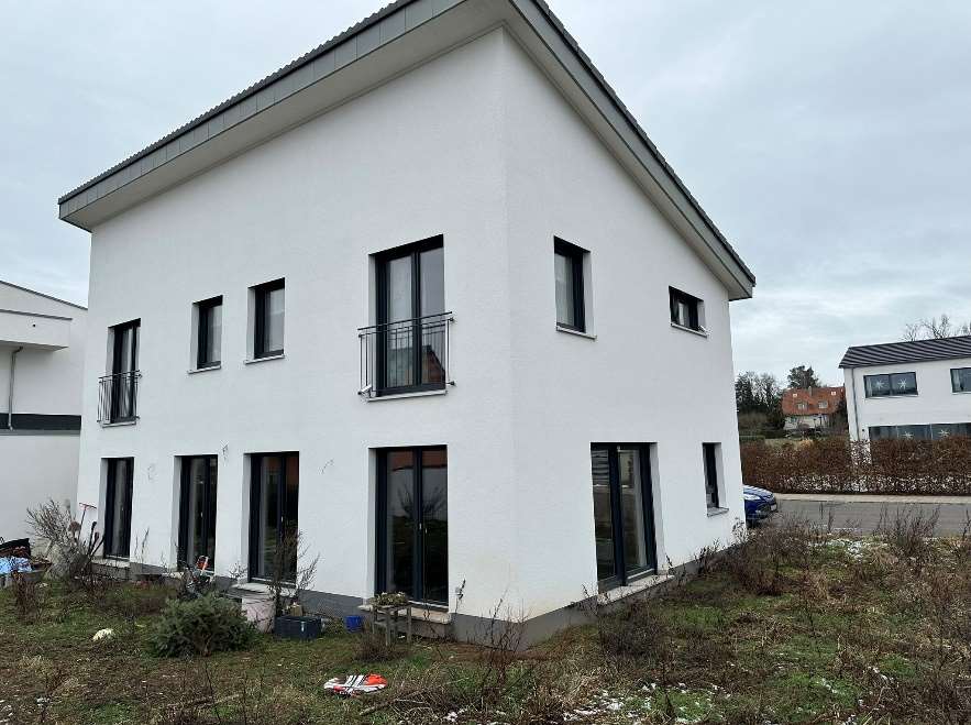 Einfamilienhaus in Cadolzburg, Pfalzhausweg 13, Außenansicht der Seitenfassade mit weißen Wänden, dunklen Fenstern und Balkonen, unberäumter Vorgarten
