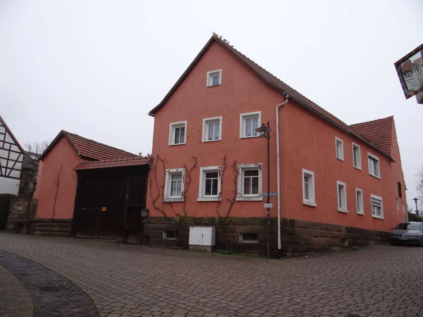 Rotes Einfamilienhaus mit Satteldach und Steinsockel, Eingangsbereich mit Garage, Schloßstraße 2, Ebenhausen