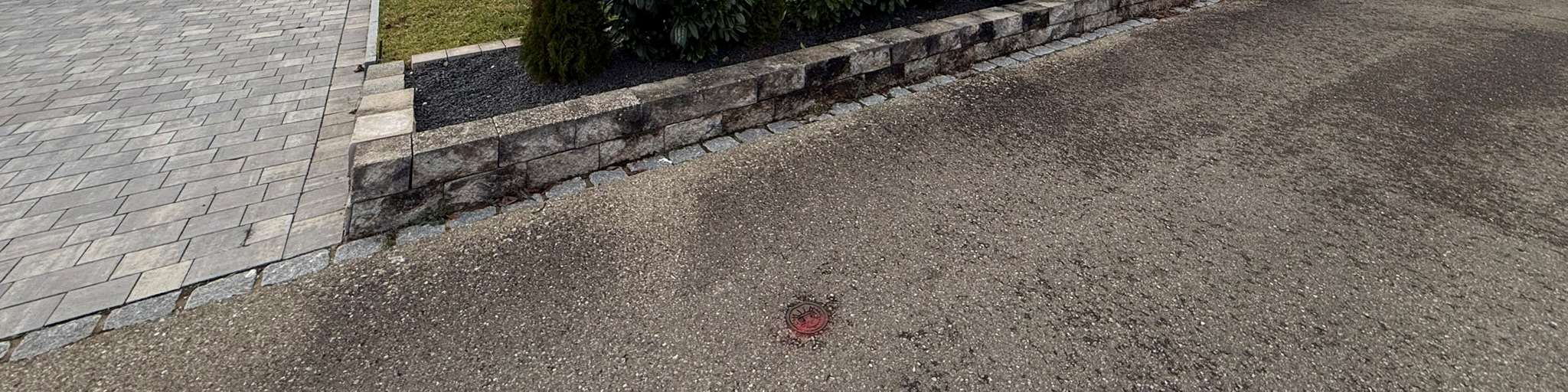 Pflasterfläche neben einer Steinmauer mit einem roten Abdeckelement auf dem Boden, Teil der Garage oder des Stellplatzes in Wilburgstetten