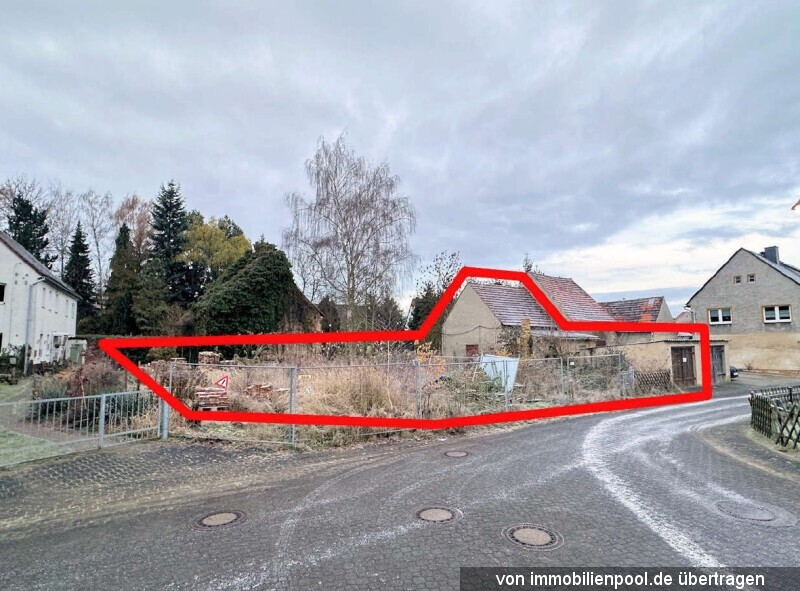 Geländestück in Wermsdorf, Friedensstraße 3, mit roter Umrandung, umzäunt, im Hintergrund Gebäude und Bäume unter bewölktem Himmel