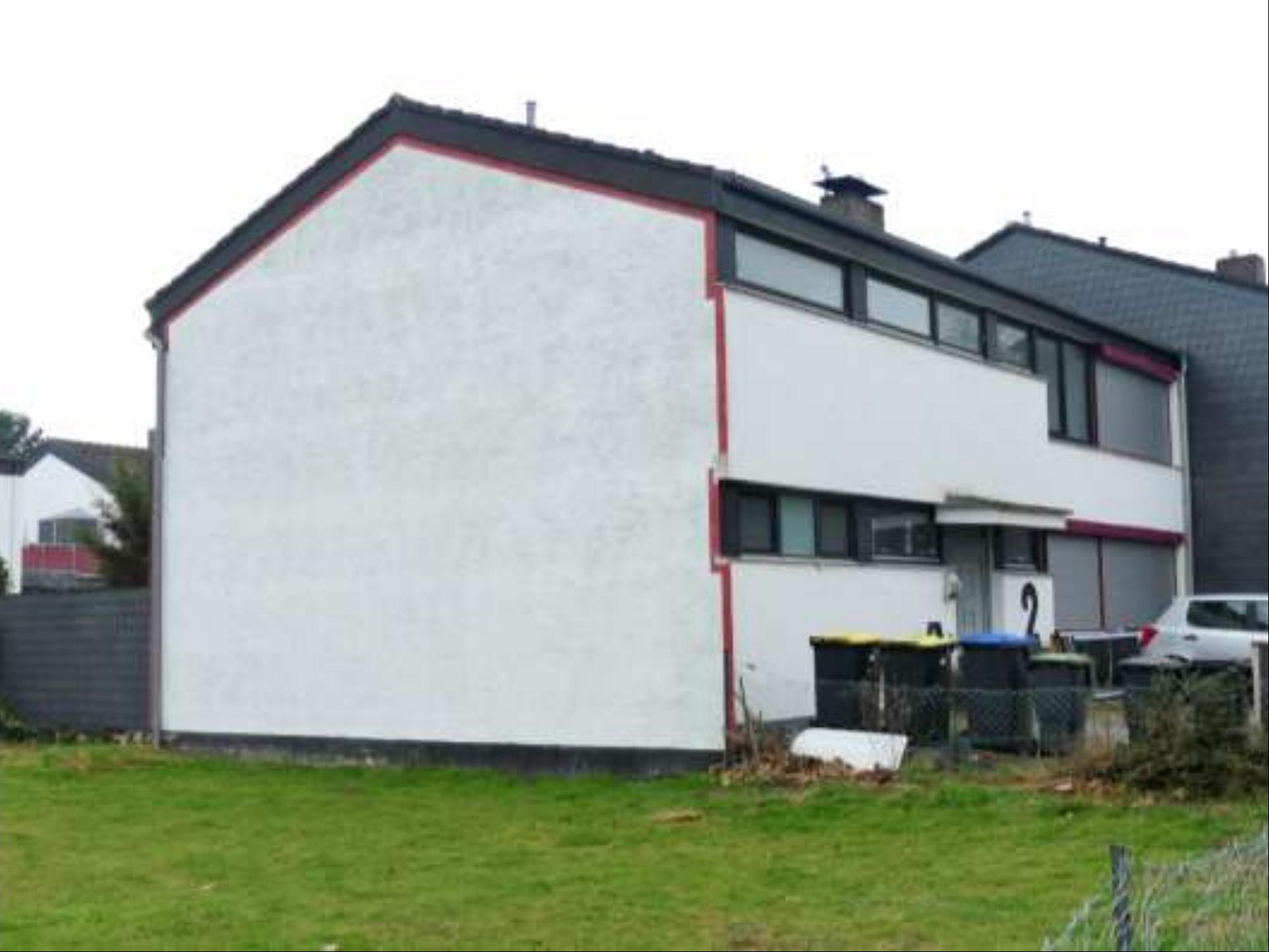 Rückansicht eines Reihenhauses mit weißer Fassade, schwarzem Dach und Gartenfläche im Vordergrund