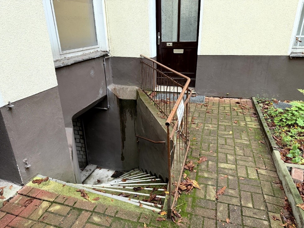 Eingangsbereich mit Tür, Metallgeländer und Treppenstufen zu einem Keller, gepflasterter Weg mit Laub, Berlin, Brüsseler Straße 21