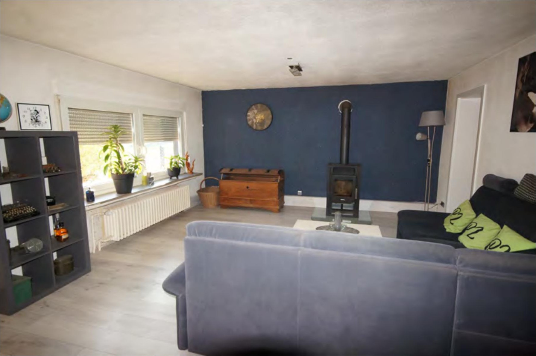 Wohnzimmer mit blauer Akzentwand, Kamin, Sofa und Pflanzen am Fenster im Reihenhaus in Brakel