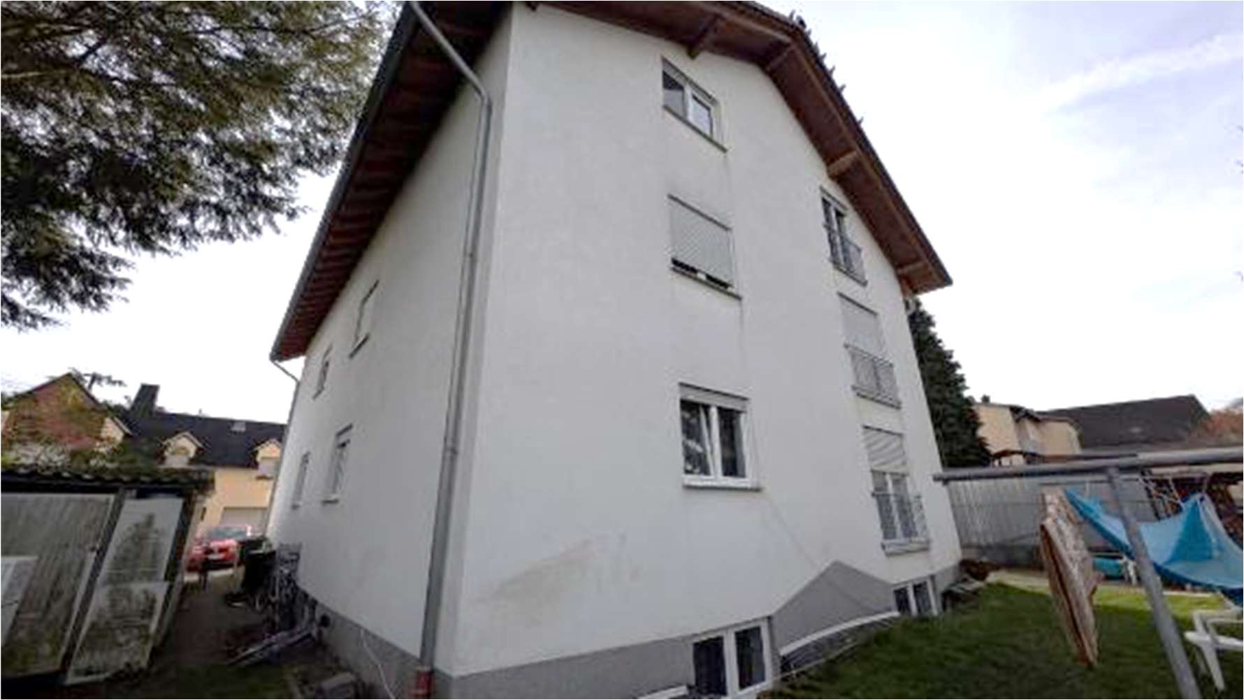 Rückansicht eines mehrstöckigen Wohnhauses mit weißen Wänden, Fenstern und angrenzendem Gartenbereich