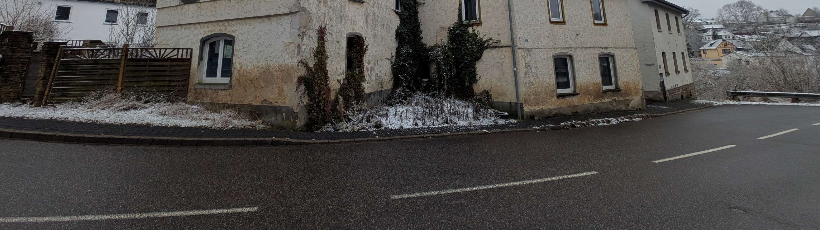 Seitenansicht eines Wohn-/Geschäftshauses in Virneburg, Hauptstraße 14, mit verwitterter Fassade, Efeu und Schnee am Straßenrand
