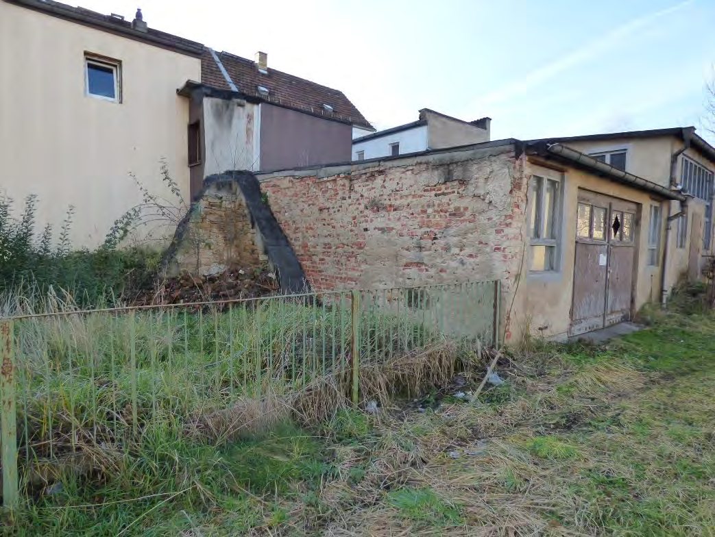 Überwuchertes Grundstück mit Metallzaun, verfallener Mauer und angrenzenden Gebäuden in Freital, Zur Lessingschule