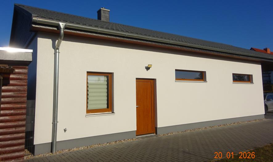 Seitenansicht eines Einfamilienhauses mit Holztür, Fenstern und grauem Dach unter klarem Himmel in Doberschütz, Heidecker Weg 67