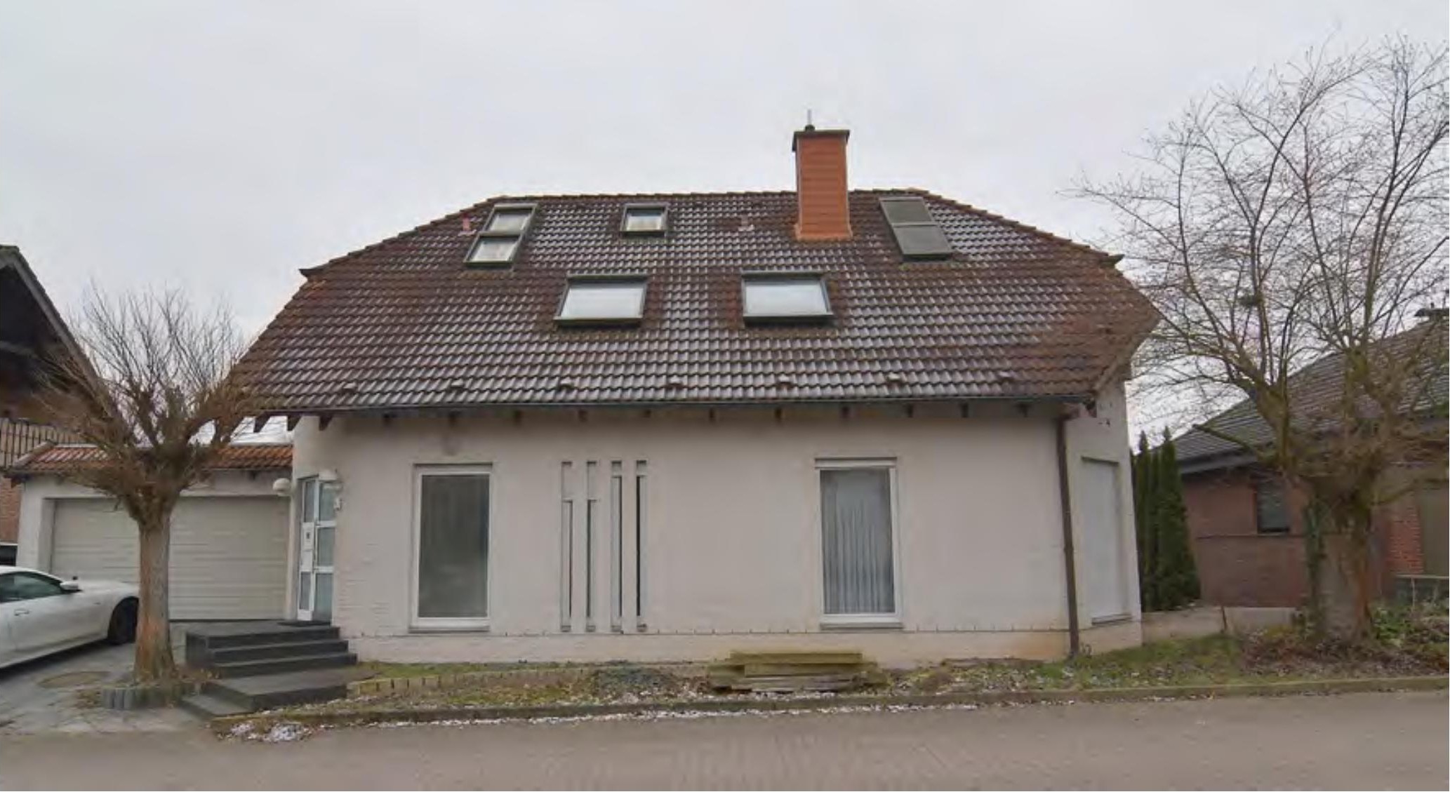 Einfamilienhaus mit Satteldach, Dachfenstern und Eingangsbereich, Garagenanbau links, kahle Bäume im Vorgarten, Ansicht von vorne