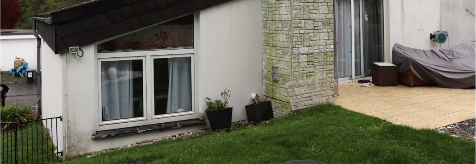 Seitenansicht eines Einfamilienhauses mit Fenster, Steinpfeiler und angrenzendem Gartenbereich mit Terrasse