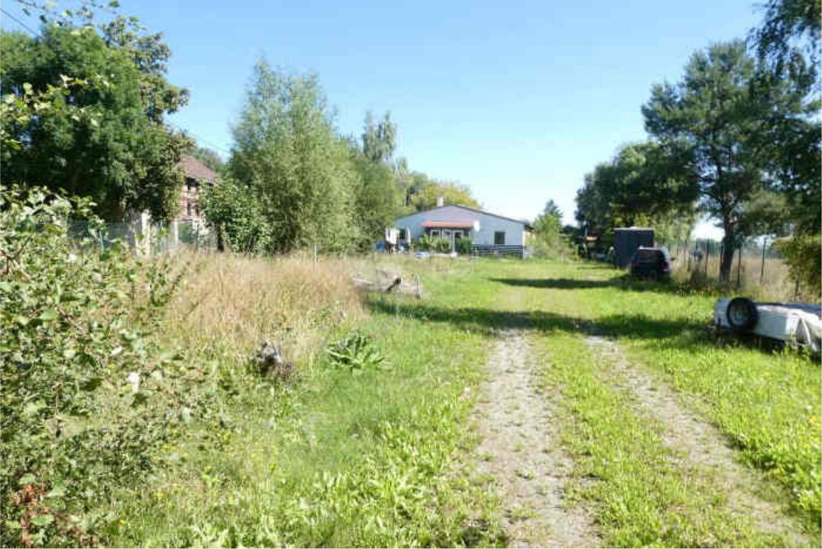 Überwuchertes Grundstück mit Gras, Bäumen und einem Weg, im Hintergrund ein Gebäude in Stadtilm, Lohmühlenweg 22