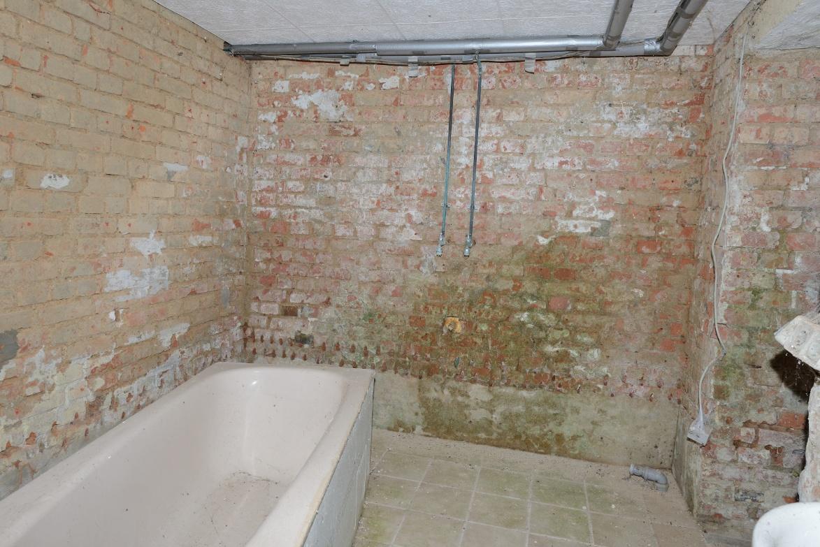 Badezimmer mit freiliegenden Ziegelwänden, Badewanne, Fliesenboden und sichtbaren Rohrleitungen
