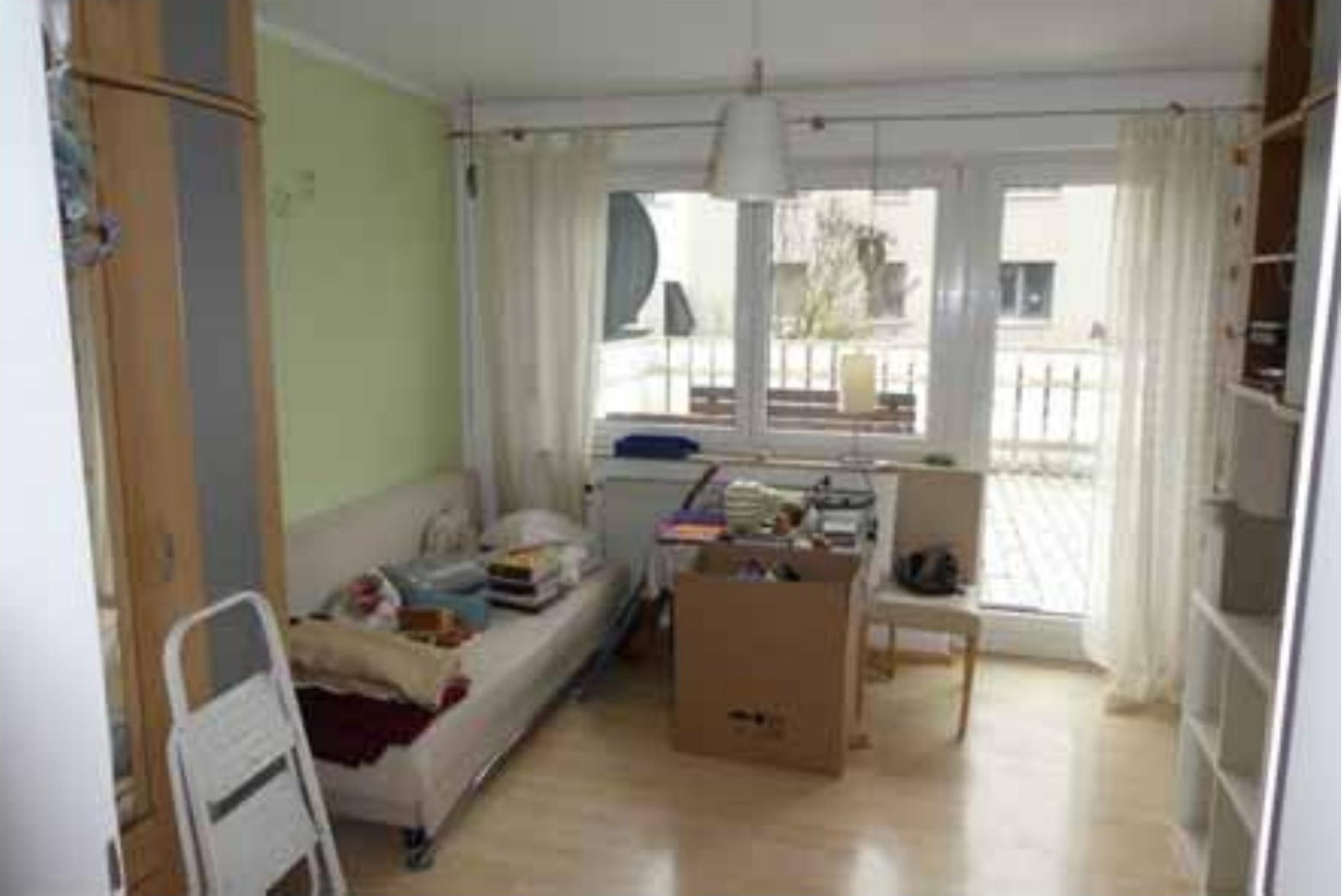Wohnbereich mit Sofa, Kartons und Möbeln, Blick auf Balkon, hellgrüne Wand, Holzboden