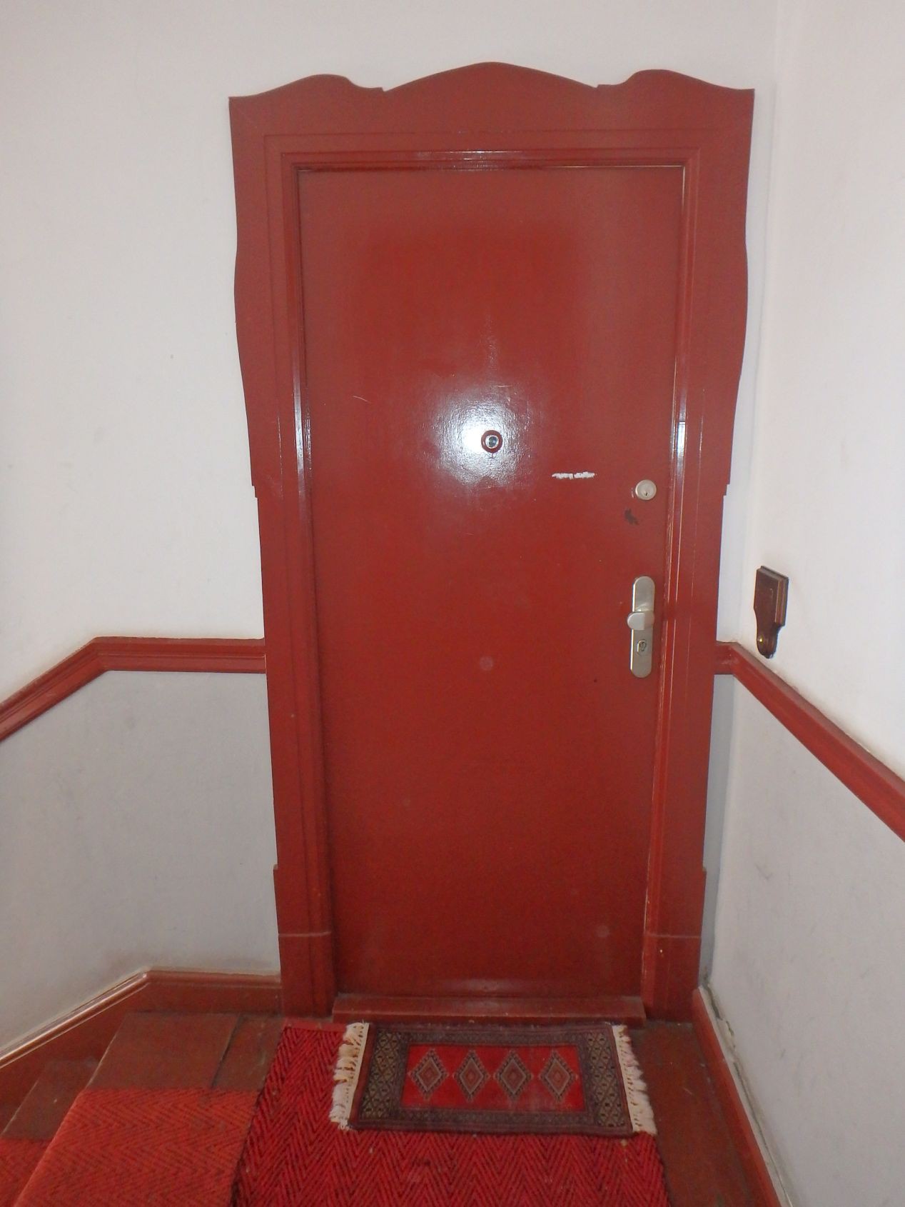 Rote Eingangstür mit passendem Rahmen und Teppich, Treppenhaus im Hintergrund, Berlin, Leibnizstraße 70