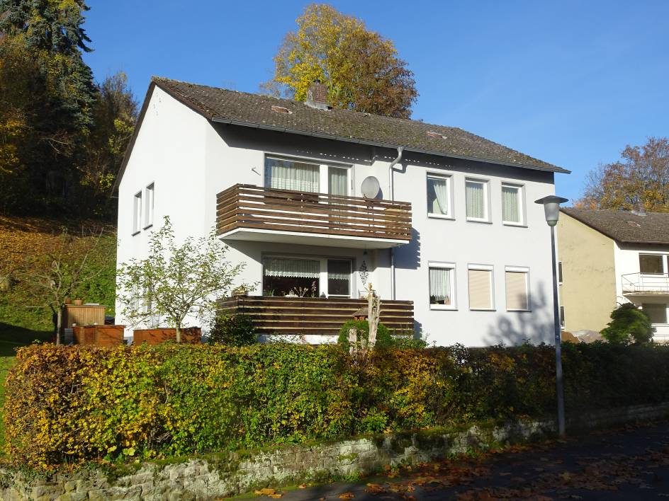 Zweifamilienhaus in Bad Sooden-Allendorf, Balzerbornweg 28, mit weißer Fassade, Holzbalkonen und Vorgarten unter blauem Himmel