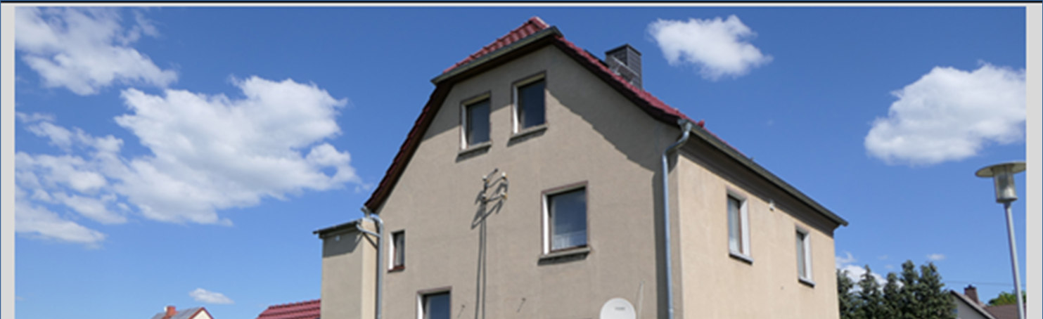 Fassade eines Zweifamilienhauses mit rotem Satteldach, mehreren Fenstern und Schornstein unter blauem Himmel