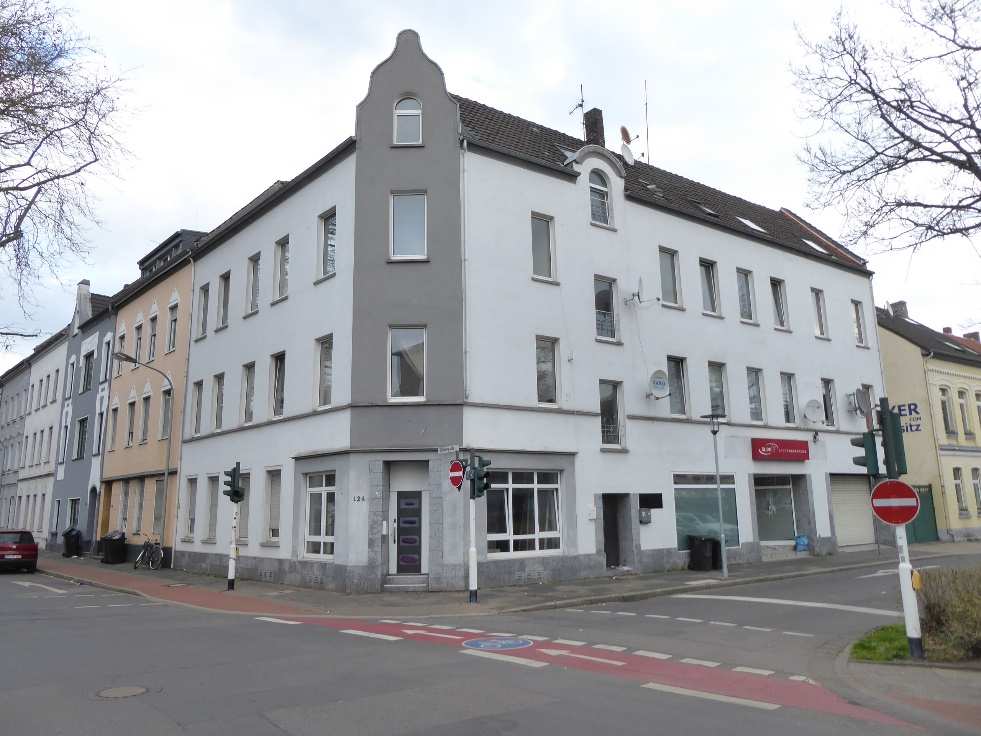Eckhaus in Krefeld, Peter-Lauten-Straße 35 / Gutenbergstraße 124, weiß-graue Fassade, Erdgeschoss mit Ladenfronten, Obergeschosse mit Fenstern, Straßenansicht mit Verkehrszeichen